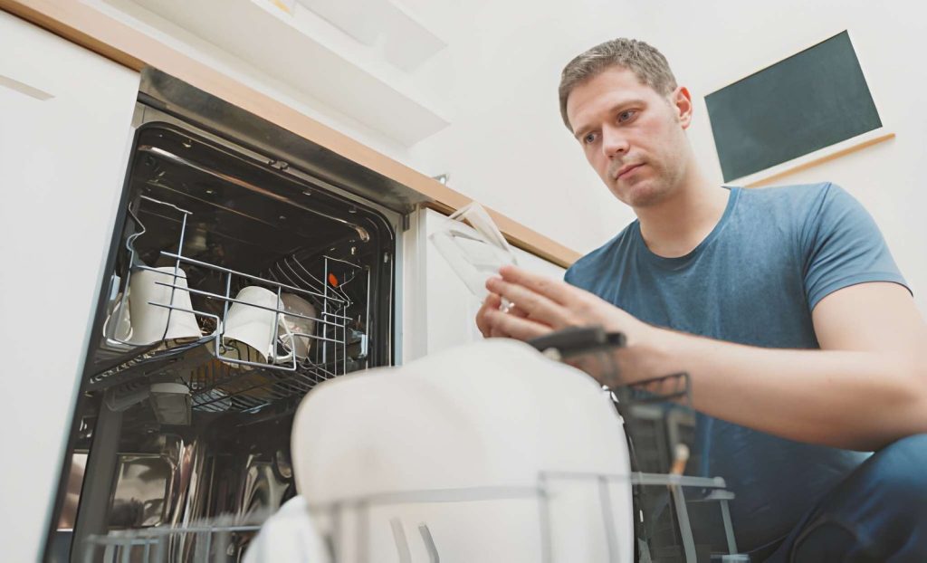 Homeowner inspecting his dishwasher to prevent leaks from the dishwasher before they cause damage