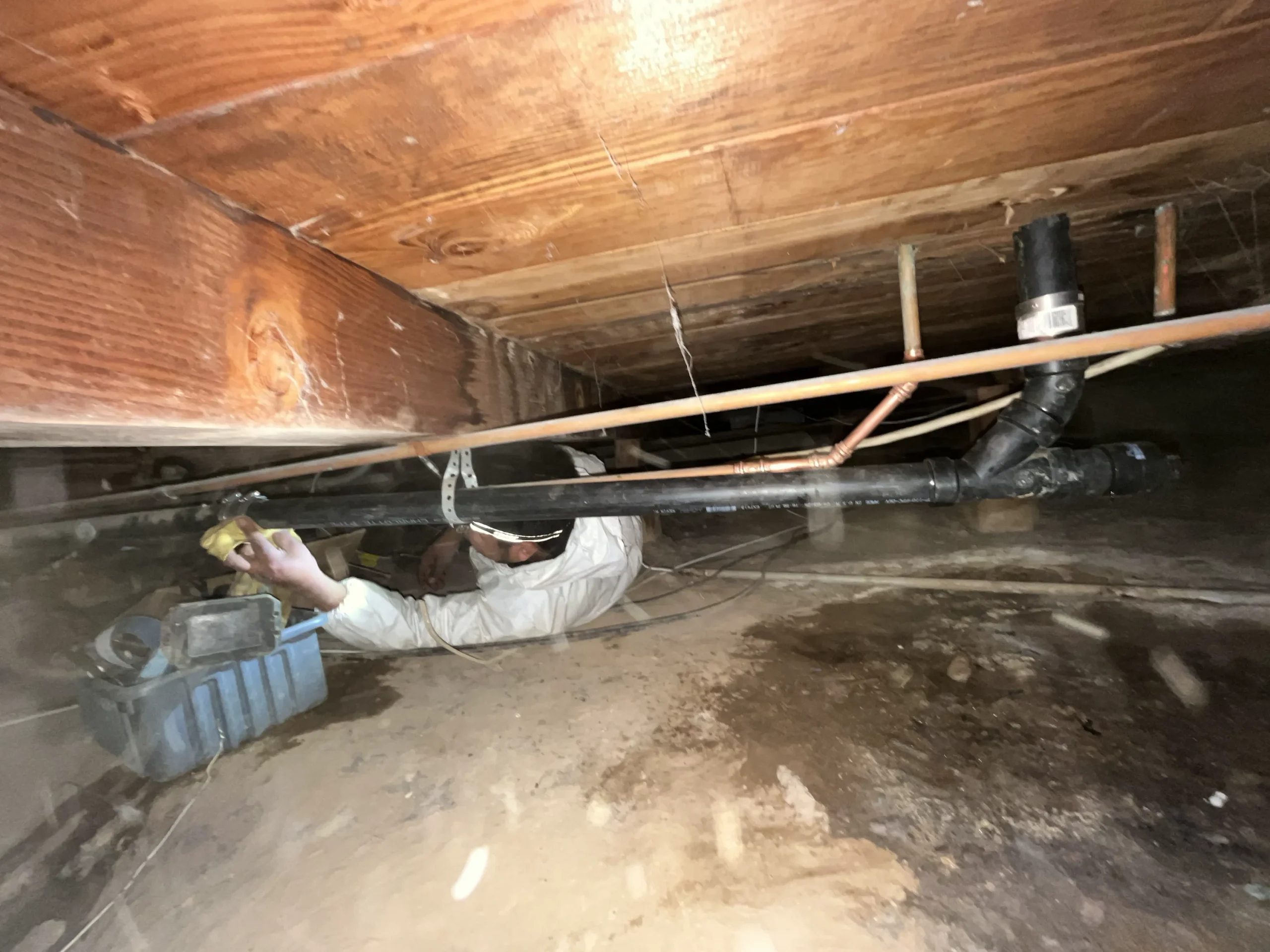 Simply Green Plumbing technician working on piping in a crawl space